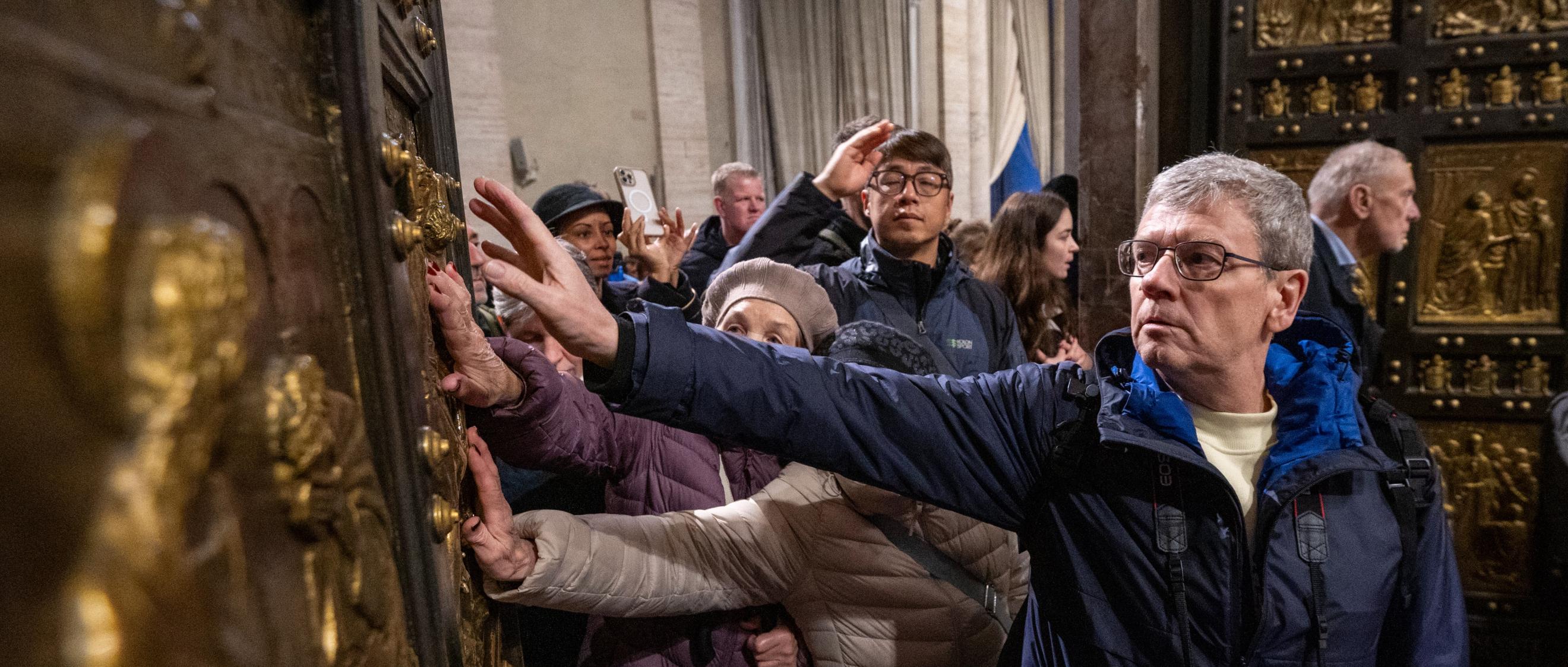 Pilger berühren  beim Durchschreiten die Heilige Pforte im Petersdom im Vatikan.