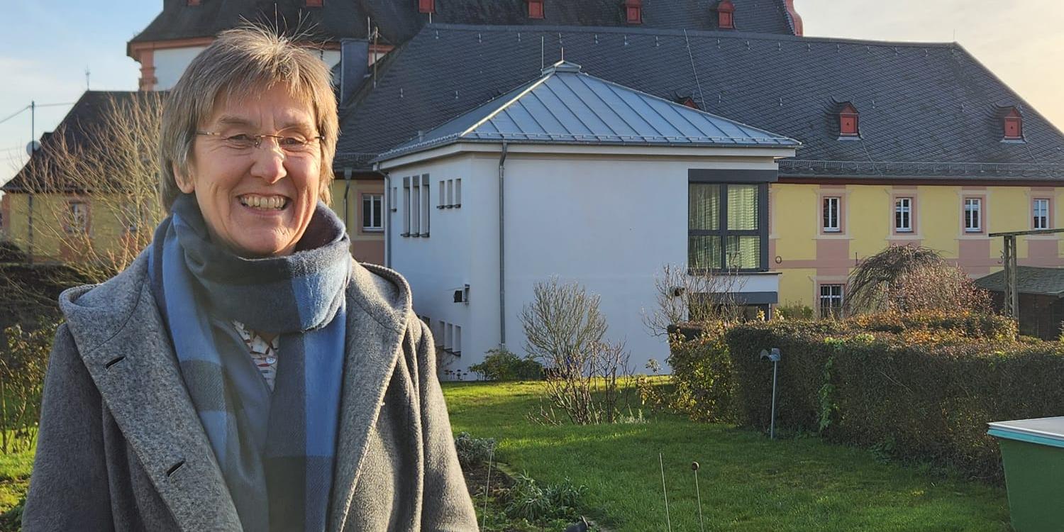 Frau steht in Garten vor Kirche mit Zwiebeltürmen im Sonnenschein. (Alt-Text erstellt mit KI-Unterstützung)