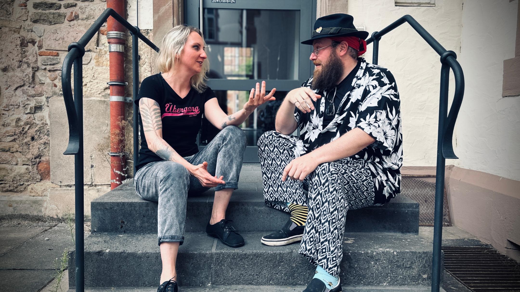 Eine Frau und ein Mann sitzen auf einer Treppe und unterhalten sich lebhaft.