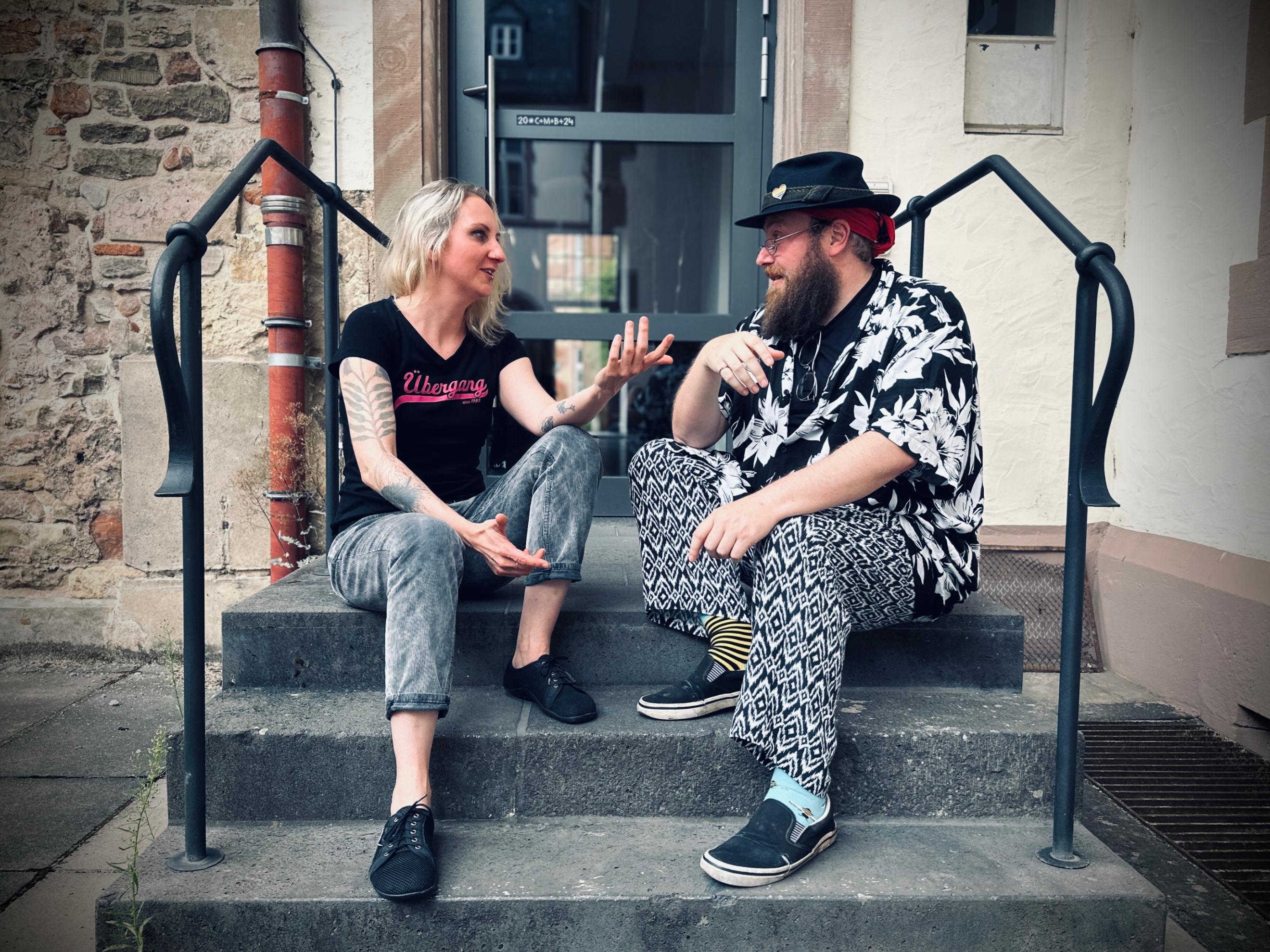 Eine Frau und ein Mann sitzen auf einer Treppe und unterhalten sich lebhaft.