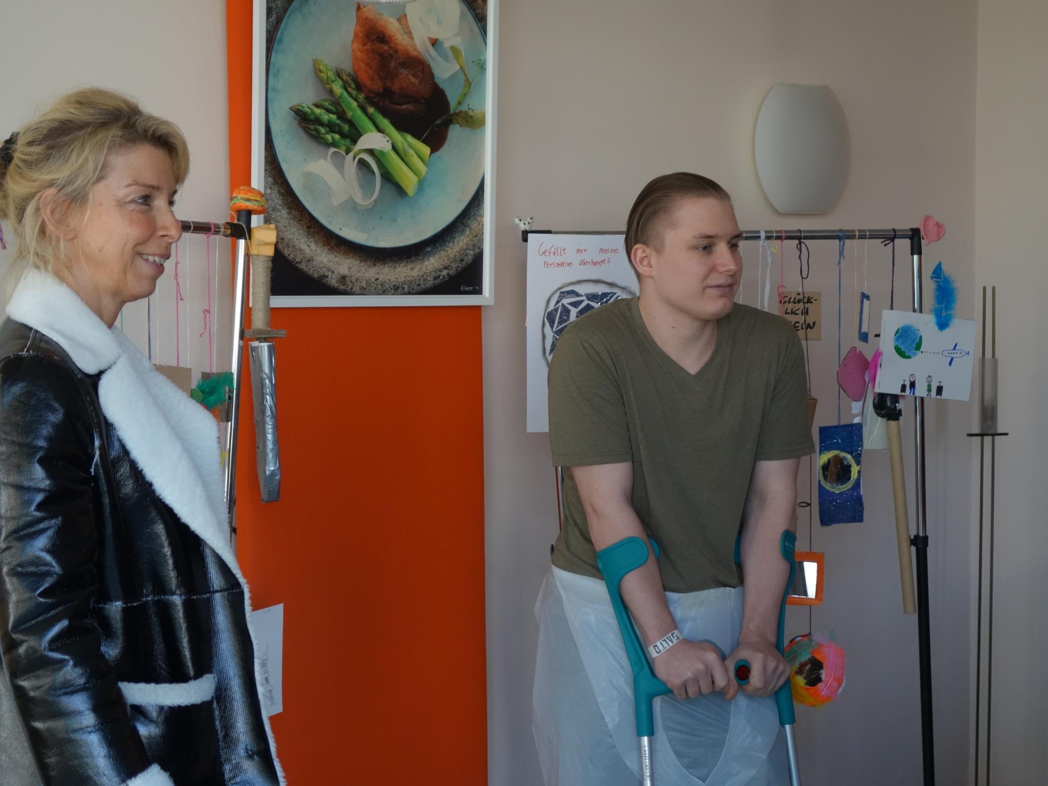 Eine Frau und ein junger Mann stehen vor einem Ständer mit spiegelnden Kunstobjekten.