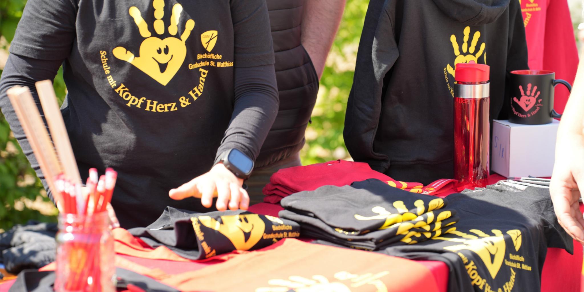 „Schule mit Kopf, Herz und Hand“: Ein Stand verkauft beim Schulfest Shirts und Utensilien mit dem Schulmotto.