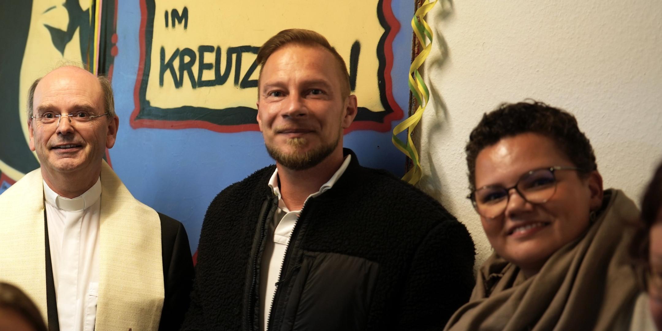 Drei Personen stehen in einem Raum.