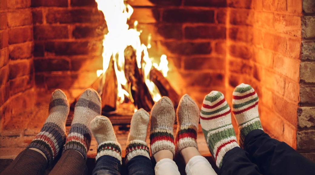 Vier paar Füße in Wollsocken werden dem Kaminfeuer gewärmt.