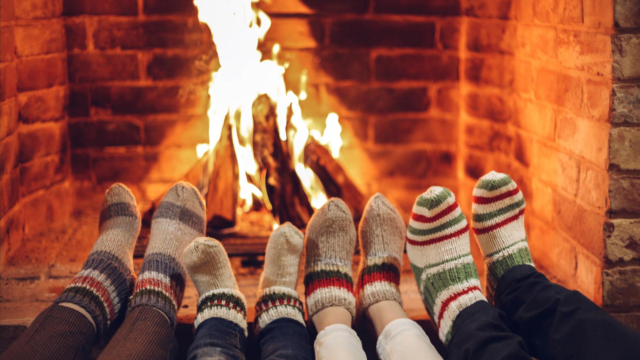 Vier paar Füße in Wollsocken werden dem Kaminfeuer gewärmt.