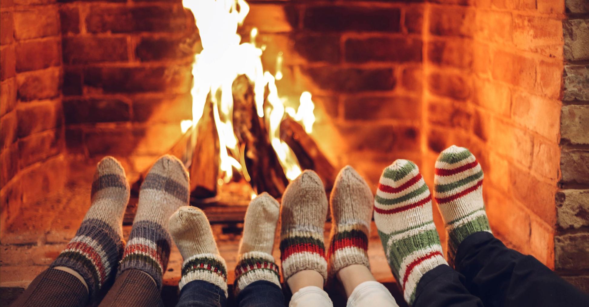Vier paar Füße in Wollsocken werden dem Kaminfeuer gewärmt.