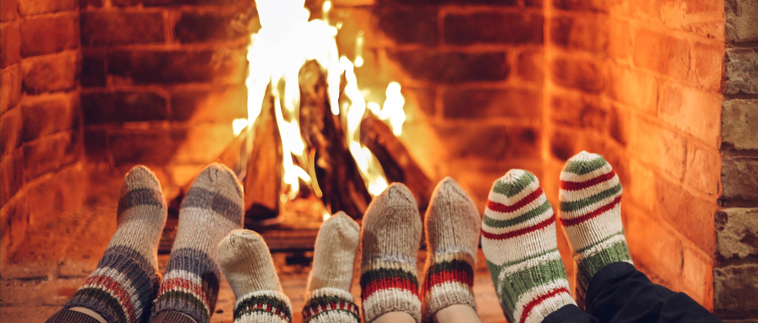 Vier paar Füße in Wollsocken werden dem Kaminfeuer gewärmt.