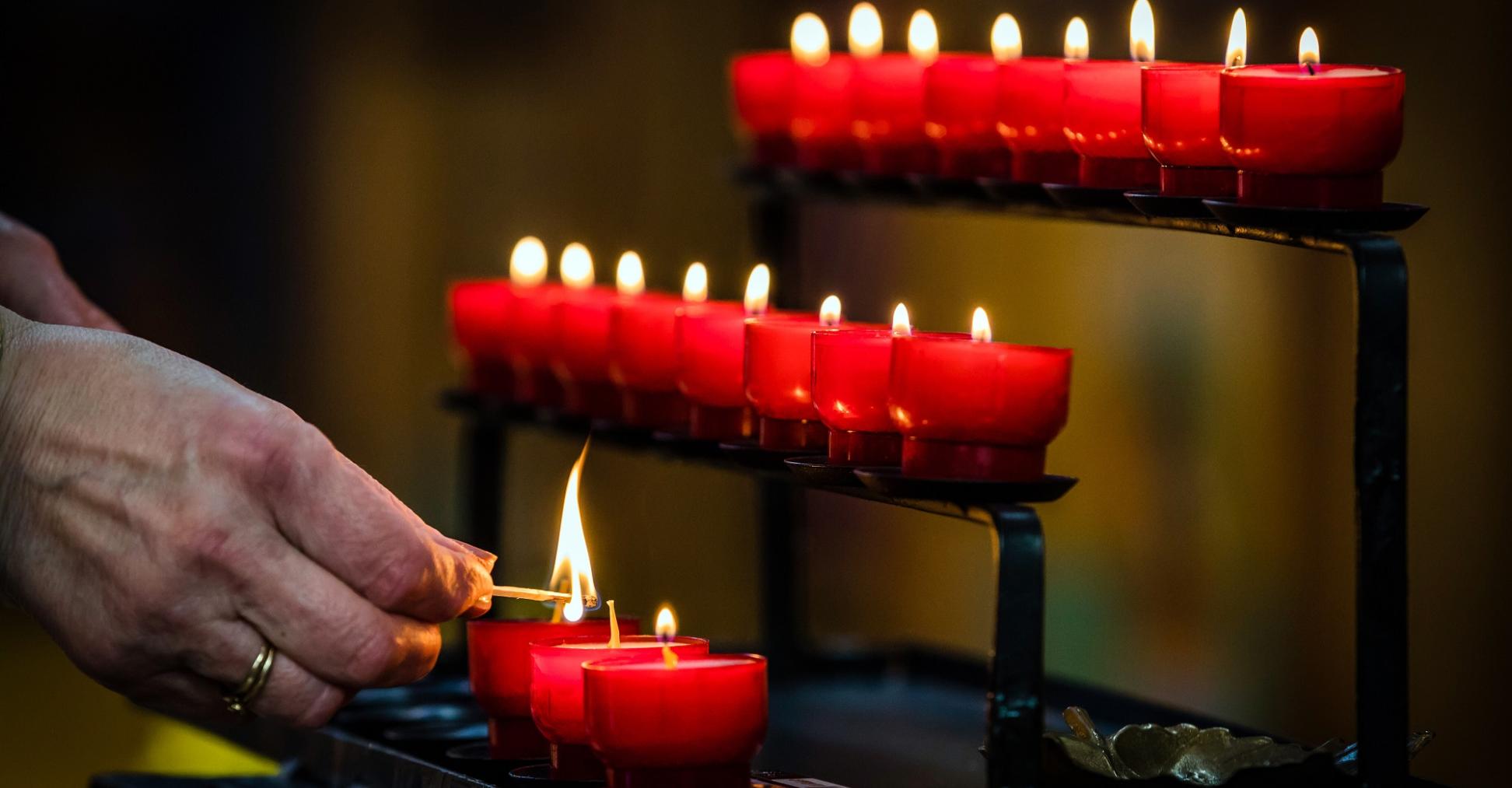 Eine Person zündet eine Kerze ion einer Kirche an.
