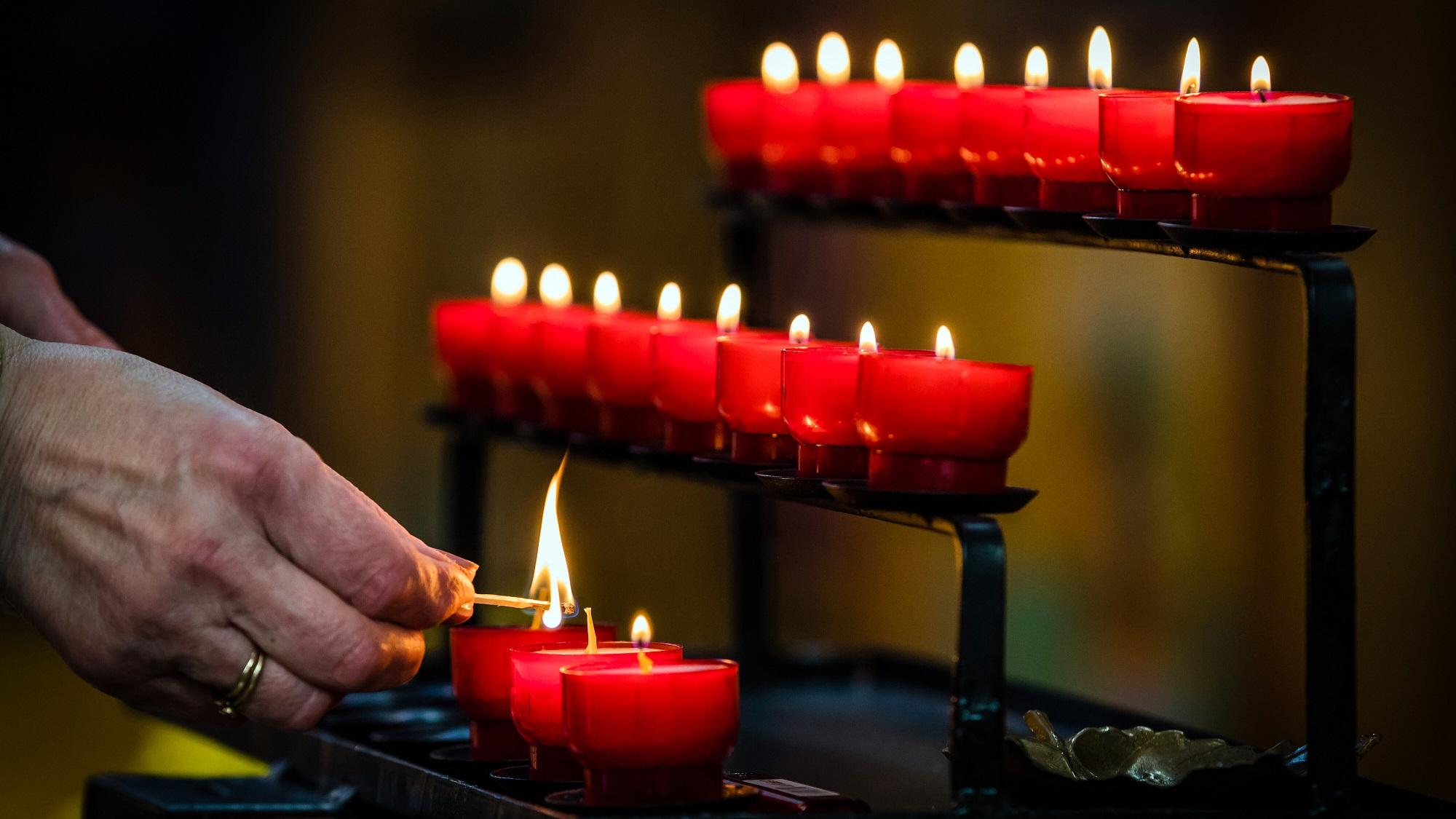 Eine Person zündet eine Kerze ion einer Kirche an.
