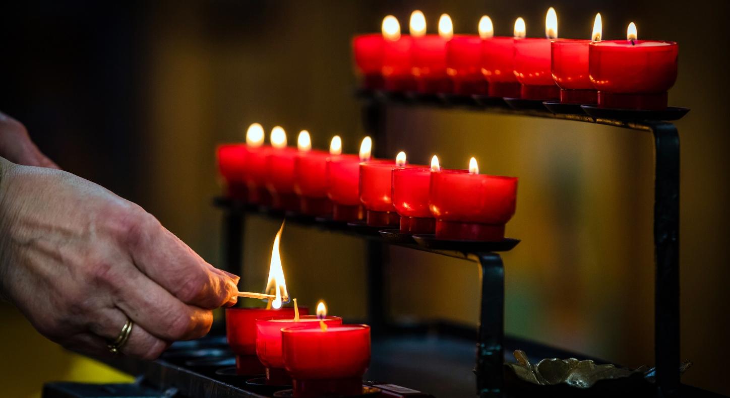 Eine Person zündet eine Kerze ion einer Kirche an.