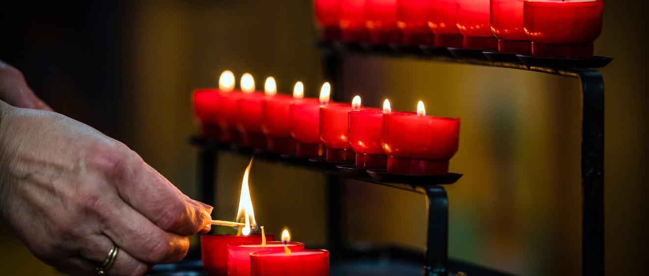 Eine Person zündet eine Kerze ion einer Kirche an.