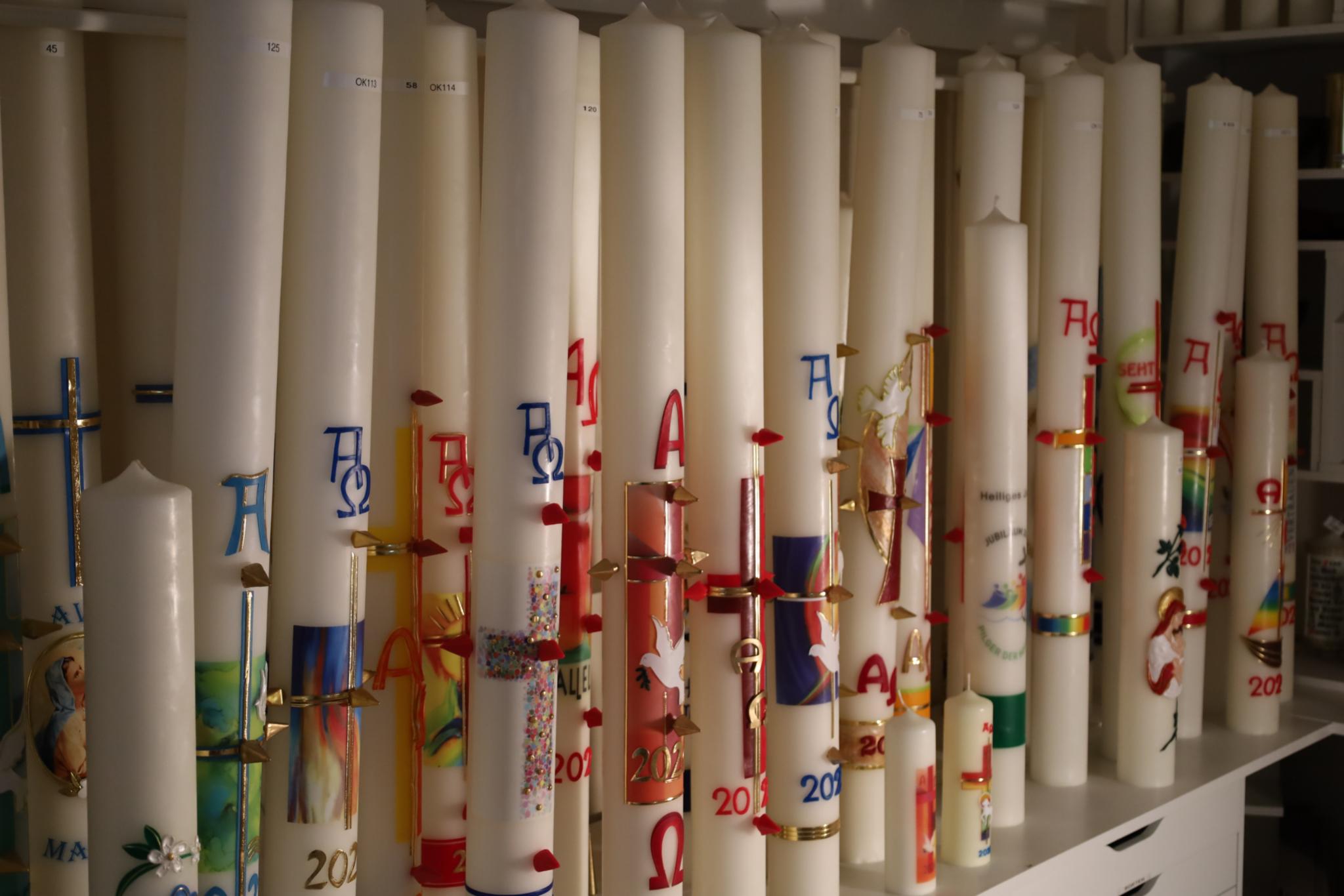 Eine Reihe hoher, bunt verzierter Kerzen mit christlichen Symbolen.