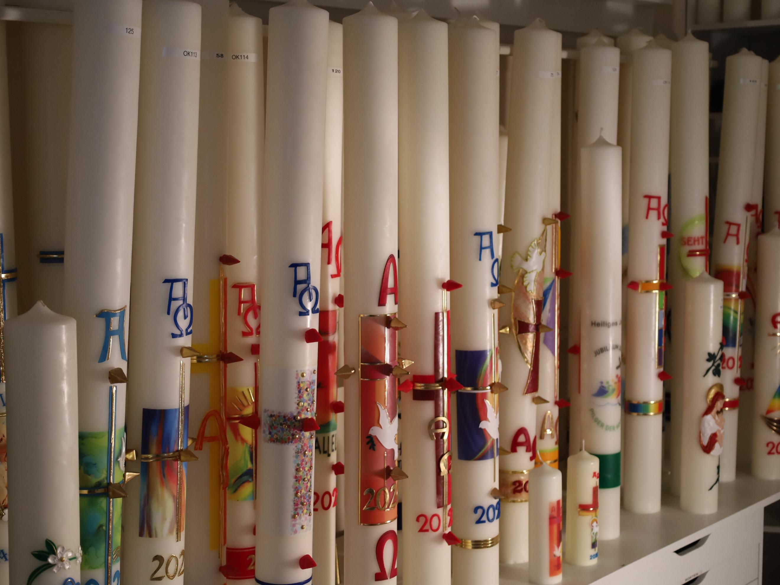 Eine Reihe hoher, bunt verzierter Kerzen mit christlichen Symbolen.