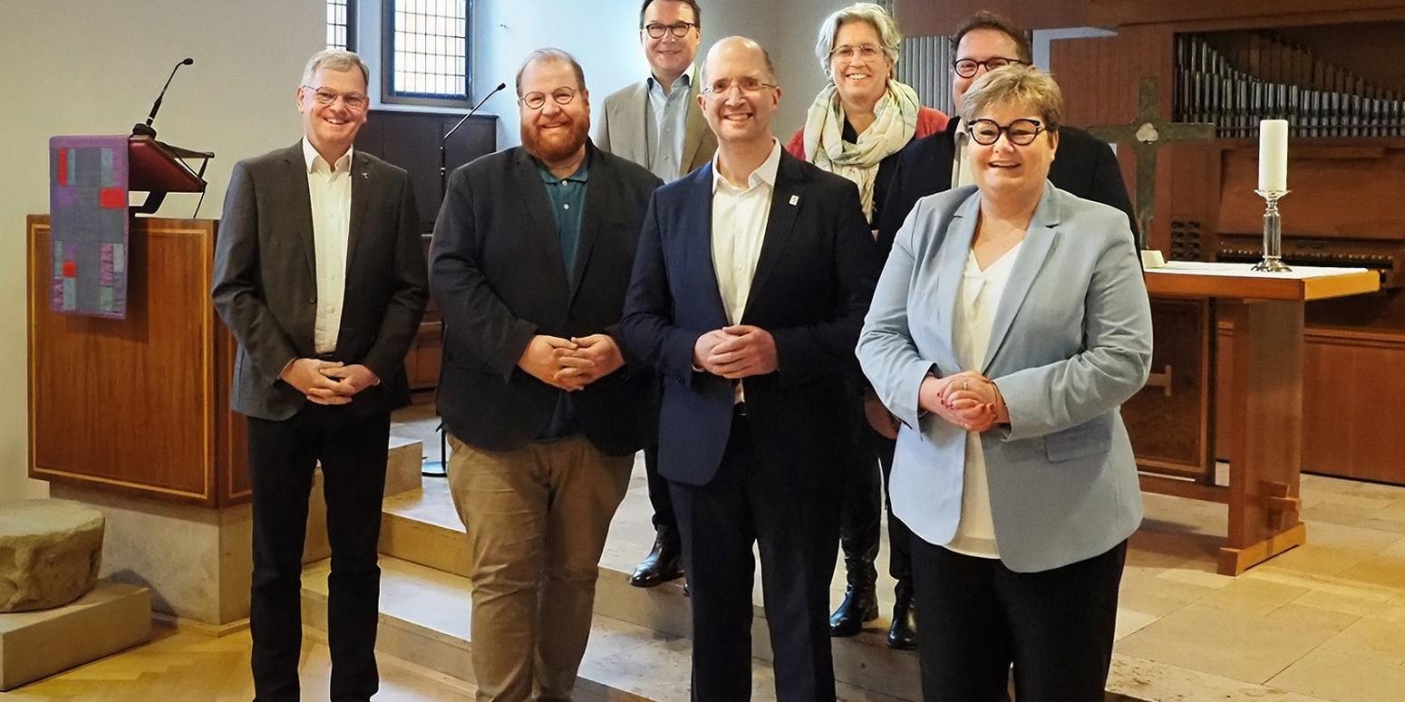 Generalvikar Dr. Ulrich Graf von Plettenberg, Bistum Trier; Markus Nöhl, Beigeordneter der Stadt Trier und Dezernent für Kultur, Tourismus und Weiterbildung; Präses Dr. Thorsten Latzel, Evangelische Kirche im Rheinland (EKiR); Staatssekretärin Bettina Brück, Ministerium für Bildung Rheinland-Pfalz (Reihe vorne v.l.); Assessor Pfarrer Thomas Luxa, Evangelischer Kirchenkreis Trier; Skriba Pfarrerin Vanessa Kluge, Evangelischer Kirchenkreis Trier; und Thomas Linnertz, Präsident der Aufsichts- und Dienstleistungsdirektion Rheinland-Pfalz in Trier (Reihe hinten, v.l.)