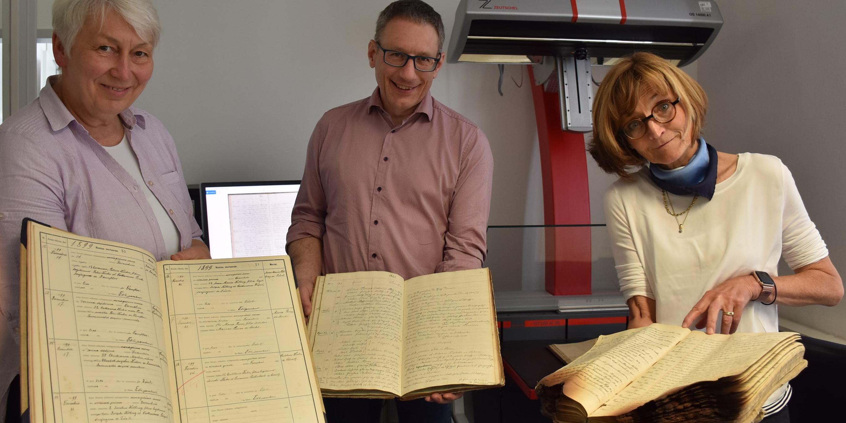 Drei Gestaltungsversionen von Kirchenbüchern aus dem Bistum zeigen Archivleiterin Monica Sinderhauf, Archivar Stefan Nicolay und Archivarin Marita Kohl (von links).