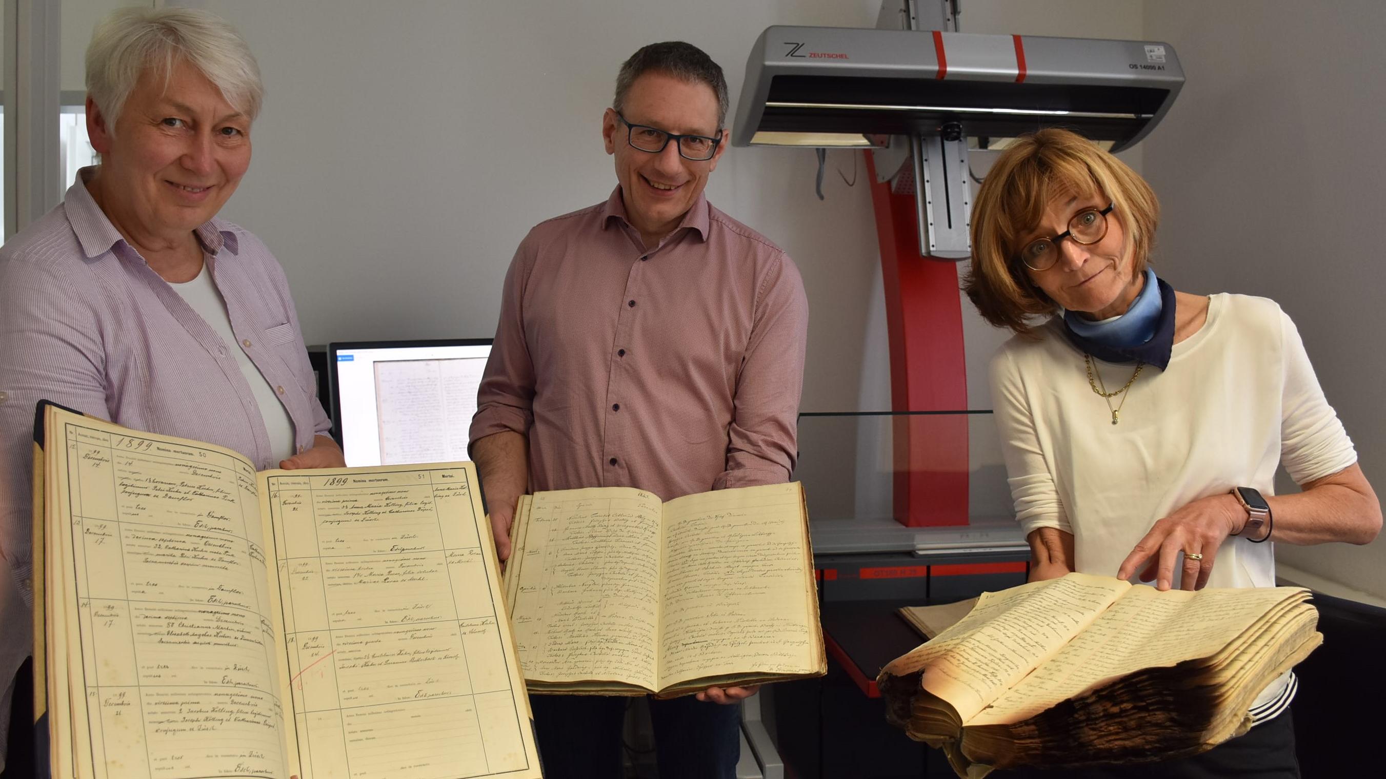 Drei Gestaltungsversionen von Kirchenbüchern aus dem Bistum zeigen Archivleiterin Monica Sinderhauf, Archivar Stefan Nicolay und Archivarin Marita Kohl (von links).