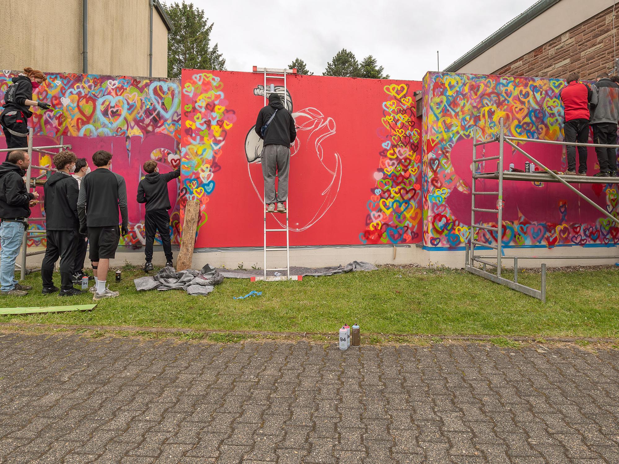 Mit Spraydosen sprühen die Jugendlichen ein zuvor gestaltetes Graffiti an die Mauern rund um die Jugendkirche MIA in Rappweiler.