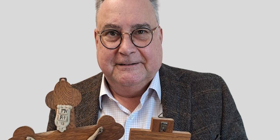 Ein Mann hat zwei alte Kreuze in der Hand und schaut in die Kamera