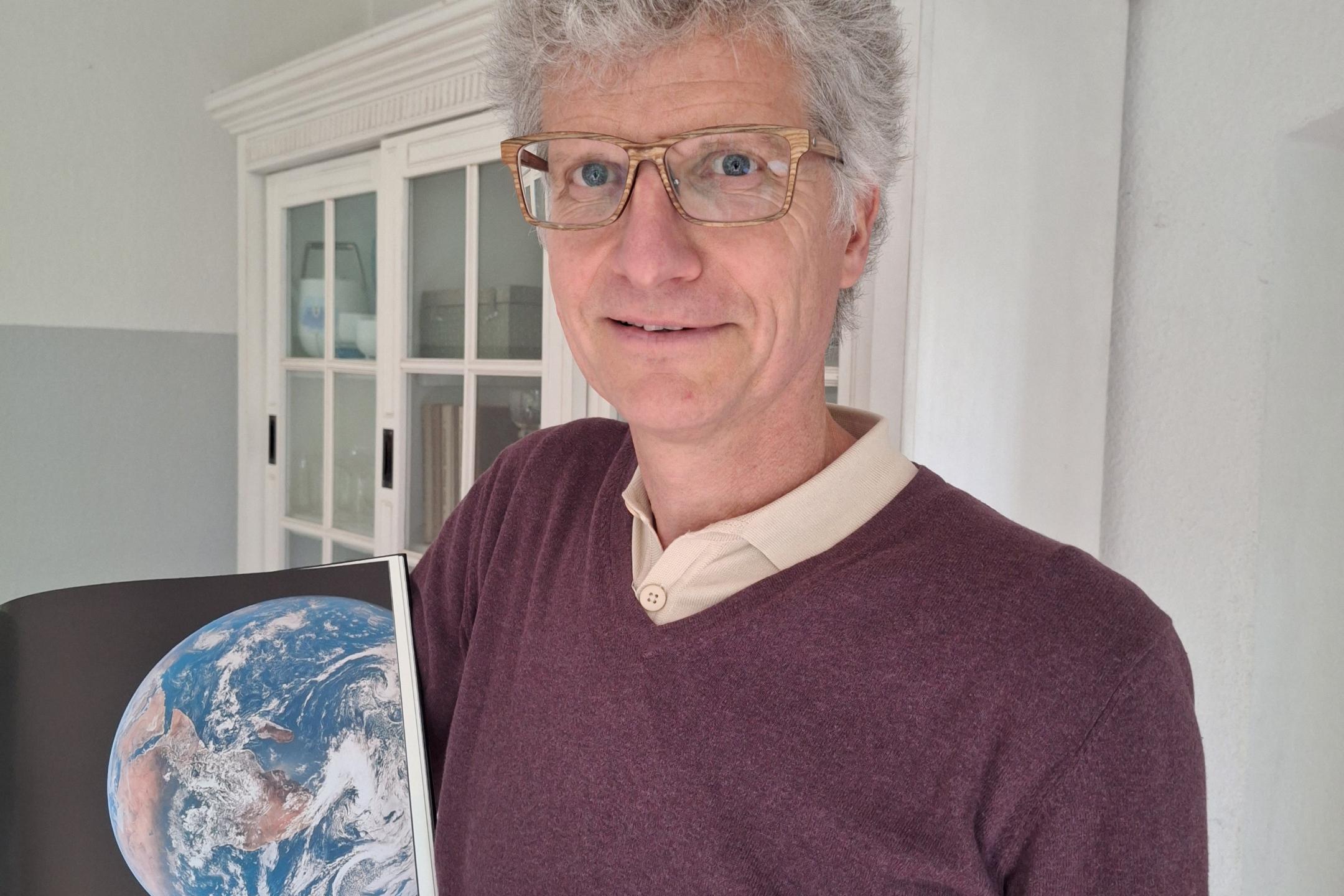 Ein Foto von Manuel Frey, wie er ein Buch zeigt, in dem die Welt abgebildet ist