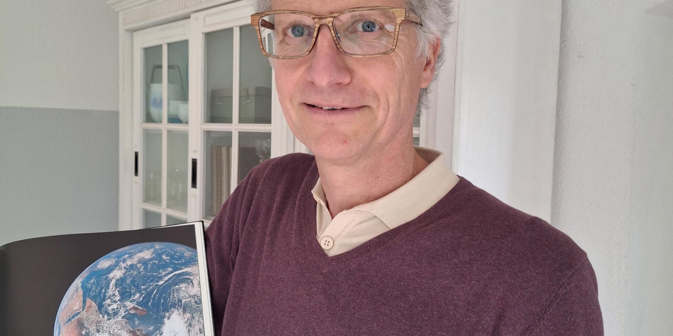 Ein Foto von Manuel Frey, wie er ein Buch zeigt, in dem die Welt abgebildet ist