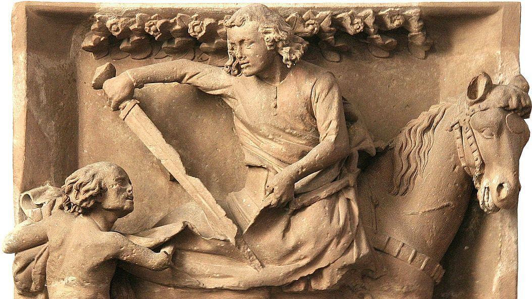 Relief aus hellem Stein: Reiter teilt seinen Mantel mit einem Bettler.  (Alt-Text erstellt mit KI-Unterstützung)