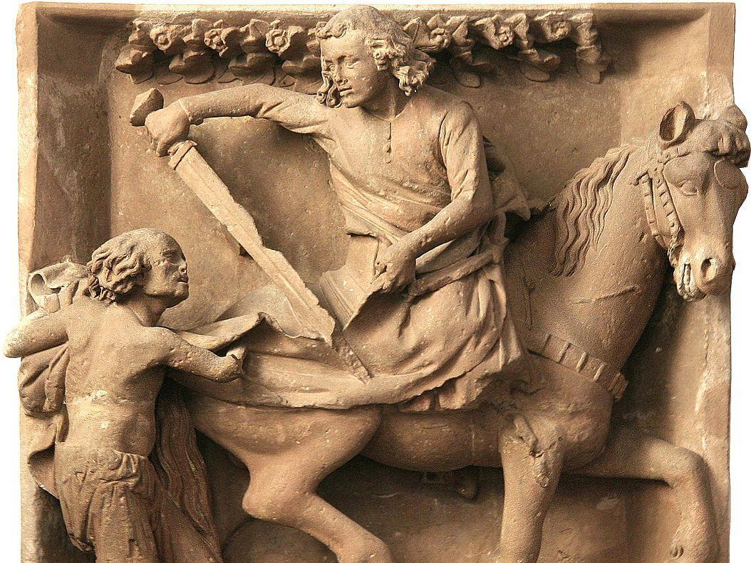 Relief aus hellem Stein: Reiter teilt seinen Mantel mit einem Bettler.  (Alt-Text erstellt mit KI-Unterstützung)