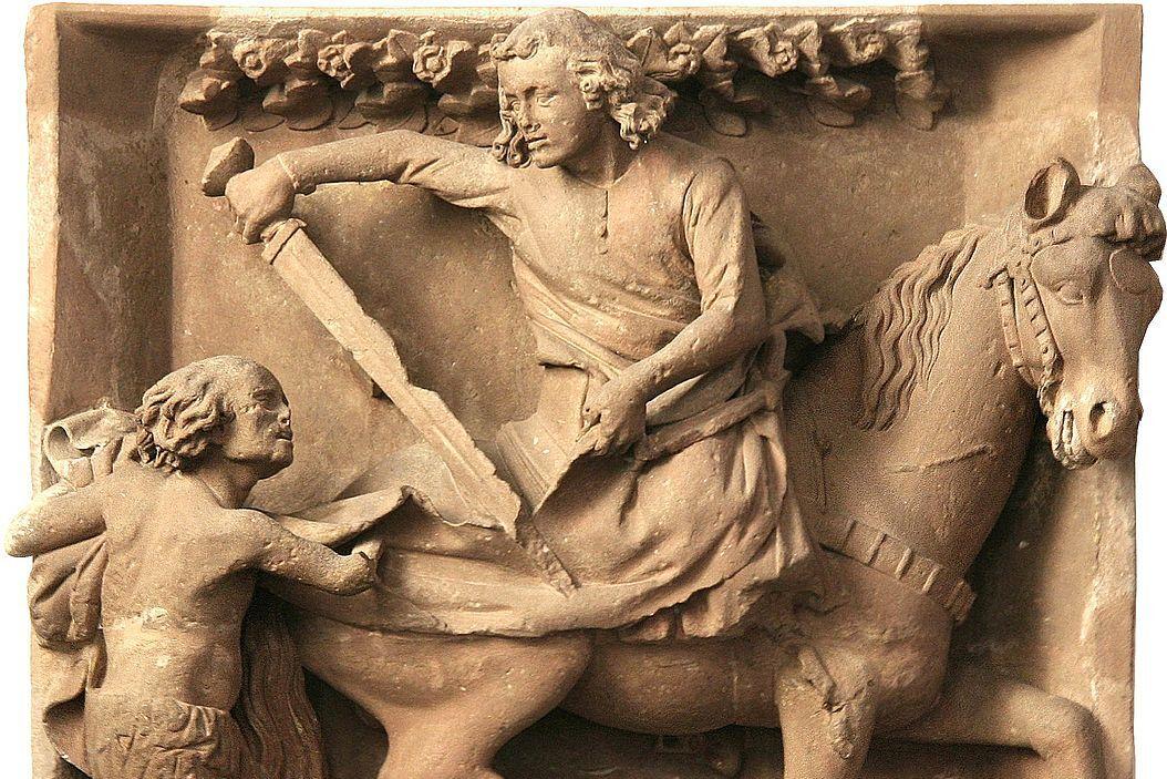 Relief aus hellem Stein: Reiter teilt seinen Mantel mit einem Bettler. (Alt-Text erstellt mit KI-Unterstützung)