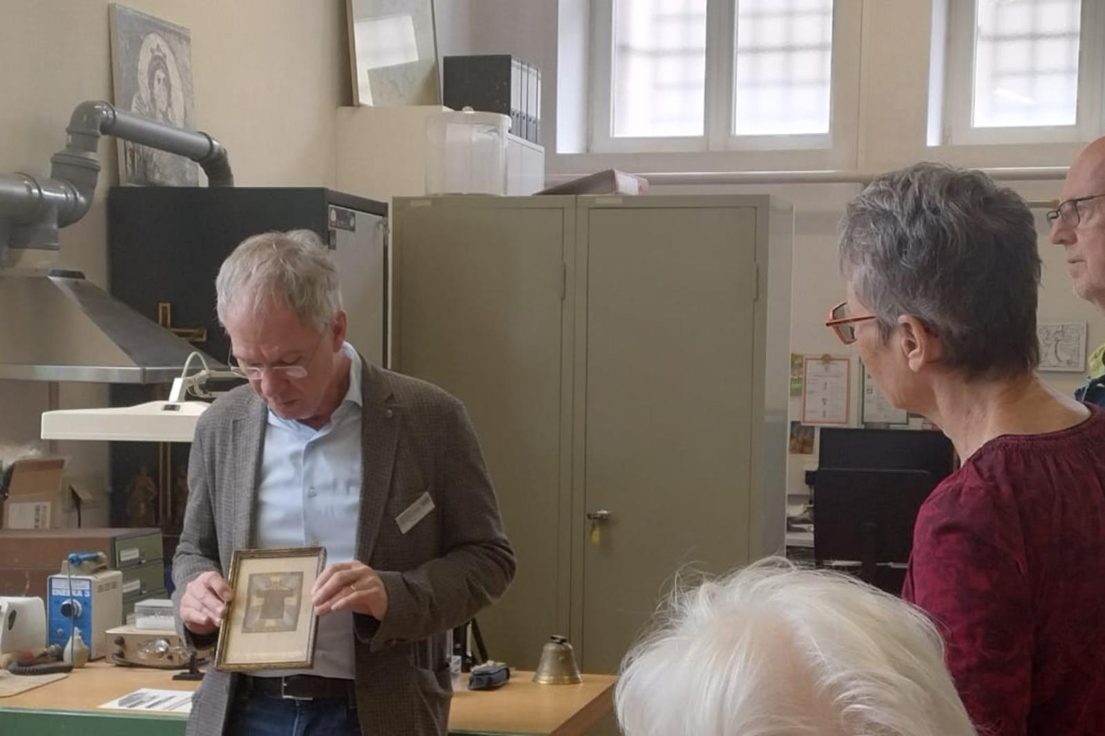 Der stellvertretende Museumsleiter und Restaurator Stefan Schu zeigt Gästen ein gerahmtes Bild.