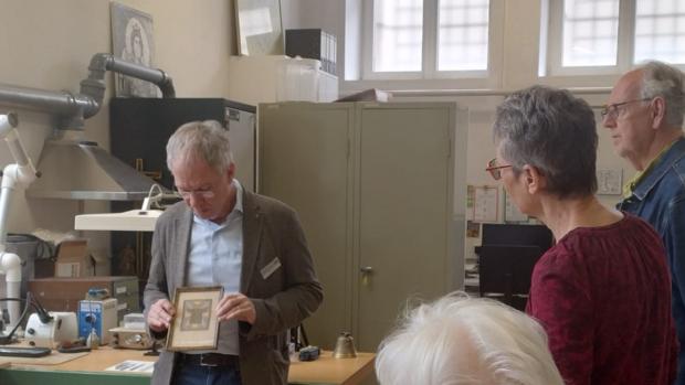 Der stellvertretende Museumsleiter und Restaurator Stefan Schu zeigt Gästen ein gerahmtes Bild.