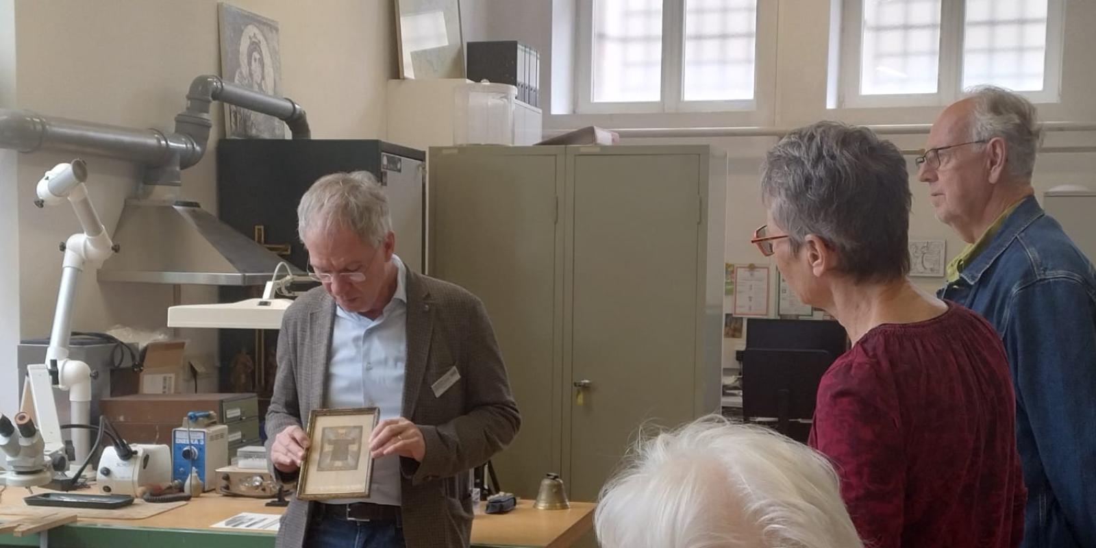 Der stellvertretende Museumsleiter und Restaurator Stefan Schu zeigt Gästen ein gerahmtes Bild.