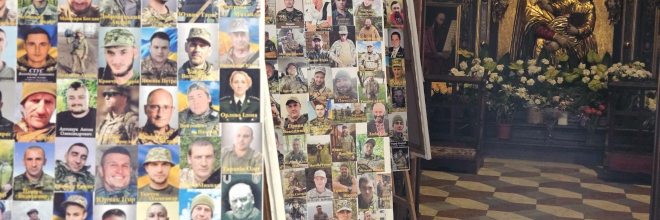 In einer Kirche stehen mehrere Staffeleien mit Fotos von Soldaten. Im Hintergrund befindet sich ein Altar mit einer goldenen Marienstatue und Blumenschmuck.