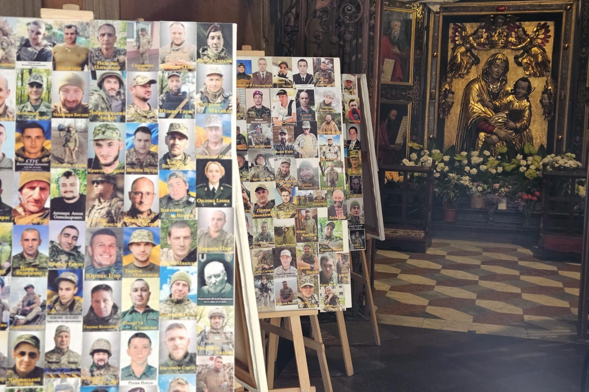 In einer Kirche stehen mehrere Staffeleien mit Fotos von Soldaten. Im Hintergrund befindet sich ein Altar mit einer goldenen Marienstatue und Blumenschmuck.