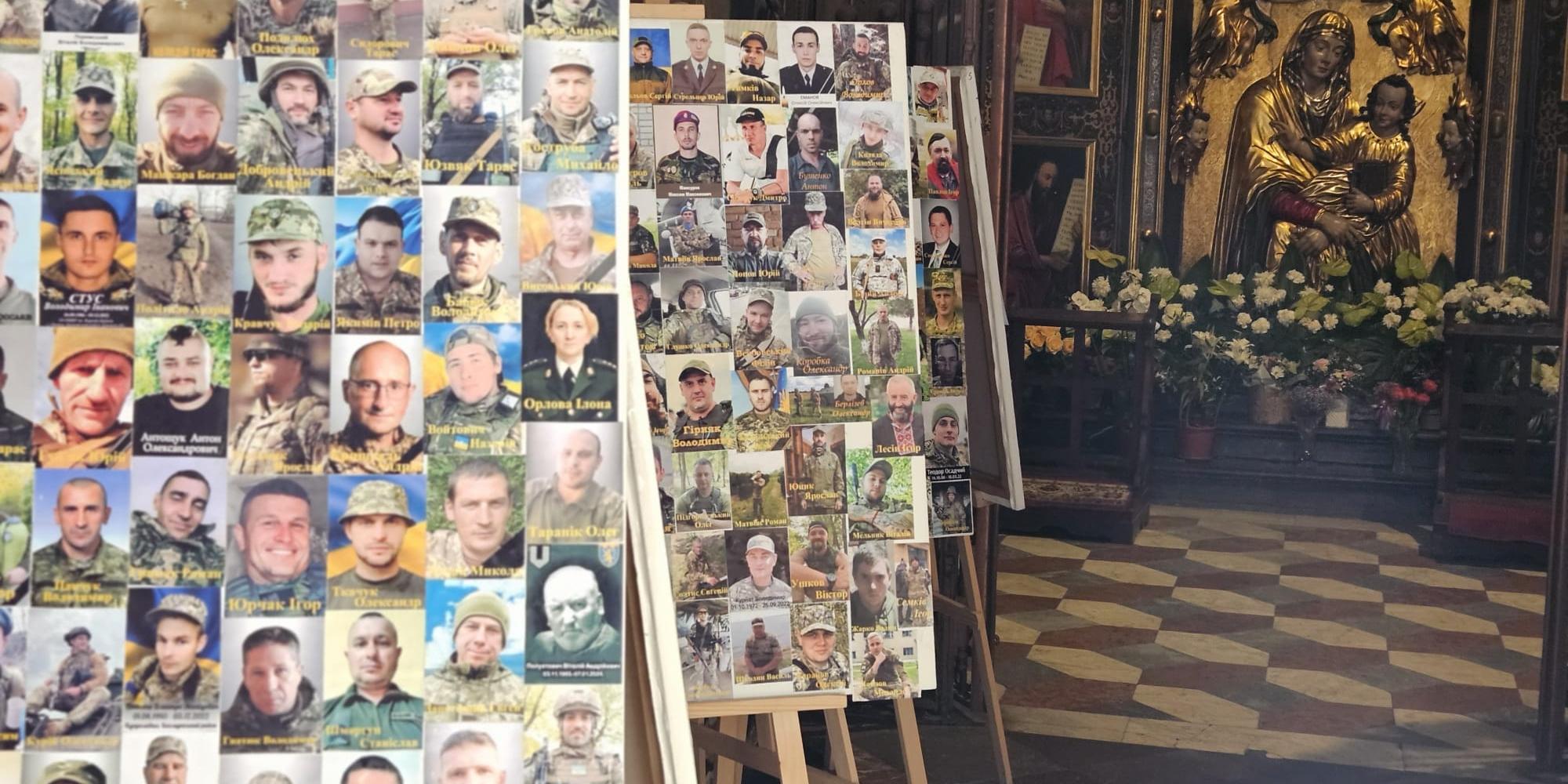 In einer Kirche stehen mehrere Staffeleien mit Fotos von Soldaten. Im Hintergrund befindet sich ein Altar mit einer goldenen Marienstatue und Blumenschmuck.