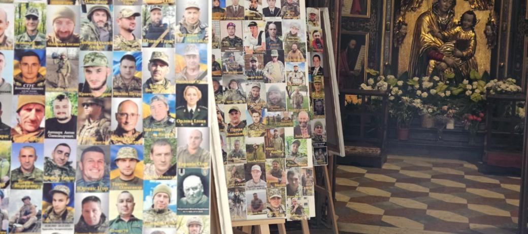 In einer Kirche stehen mehrere Staffeleien mit Fotos von Soldaten. Im Hintergrund befindet sich ein Altar mit einer goldenen Marienstatue und Blumenschmuck.