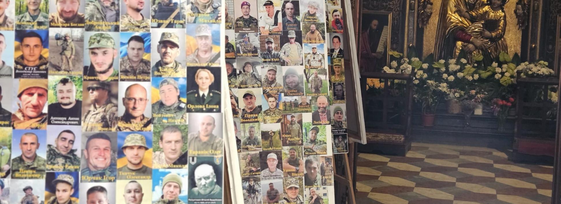 In einer Kirche stehen mehrere Staffeleien mit Fotos von Soldaten. Im Hintergrund befindet sich ein Altar mit einer goldenen Marienstatue und Blumenschmuck.