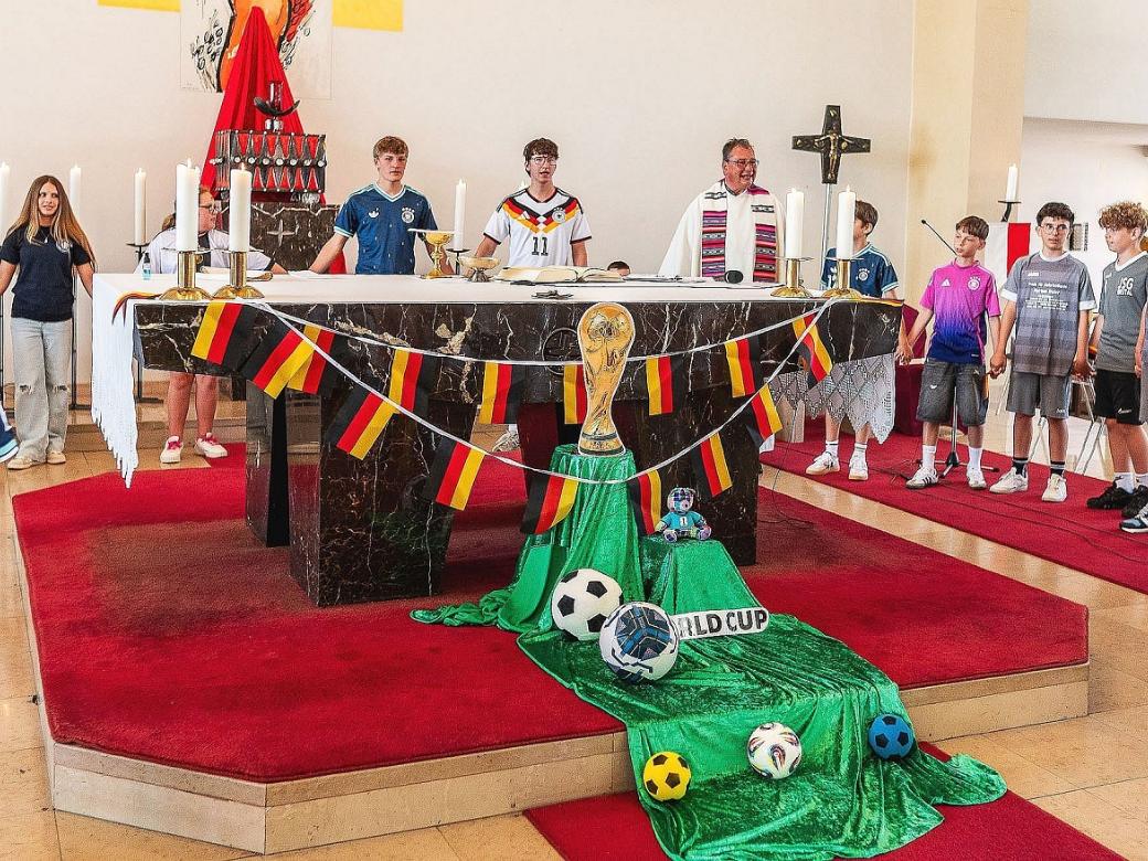 Pfarrer Peter Leick stehlt gemeinsam mit Kindern im Fußball-Dress um den passend zur WM geschmückten Altar