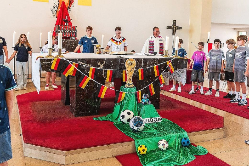 Pfarrer Peter Leick stehlt gemeinsam mit Kindern im Fußball-Dress um den passend zur WM geschmückten Altar