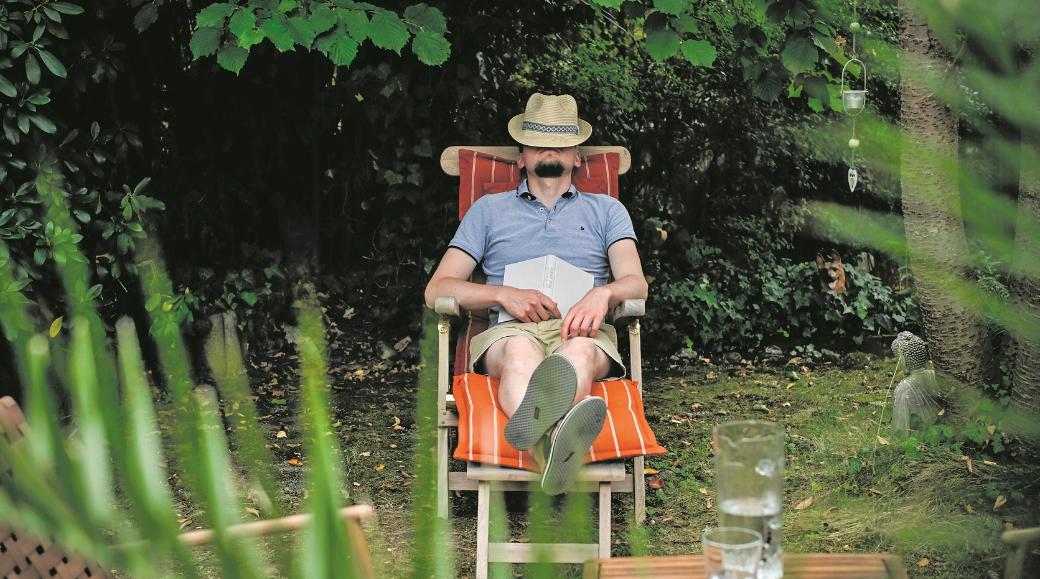 Ein Mann mit einem Hut auf dem Gesicht sitzt in einem Gartenstuhl und schläft, am 26. August 2025 in einem Garten in Bonn. Auf seinem Schoß liegt ein Buch.