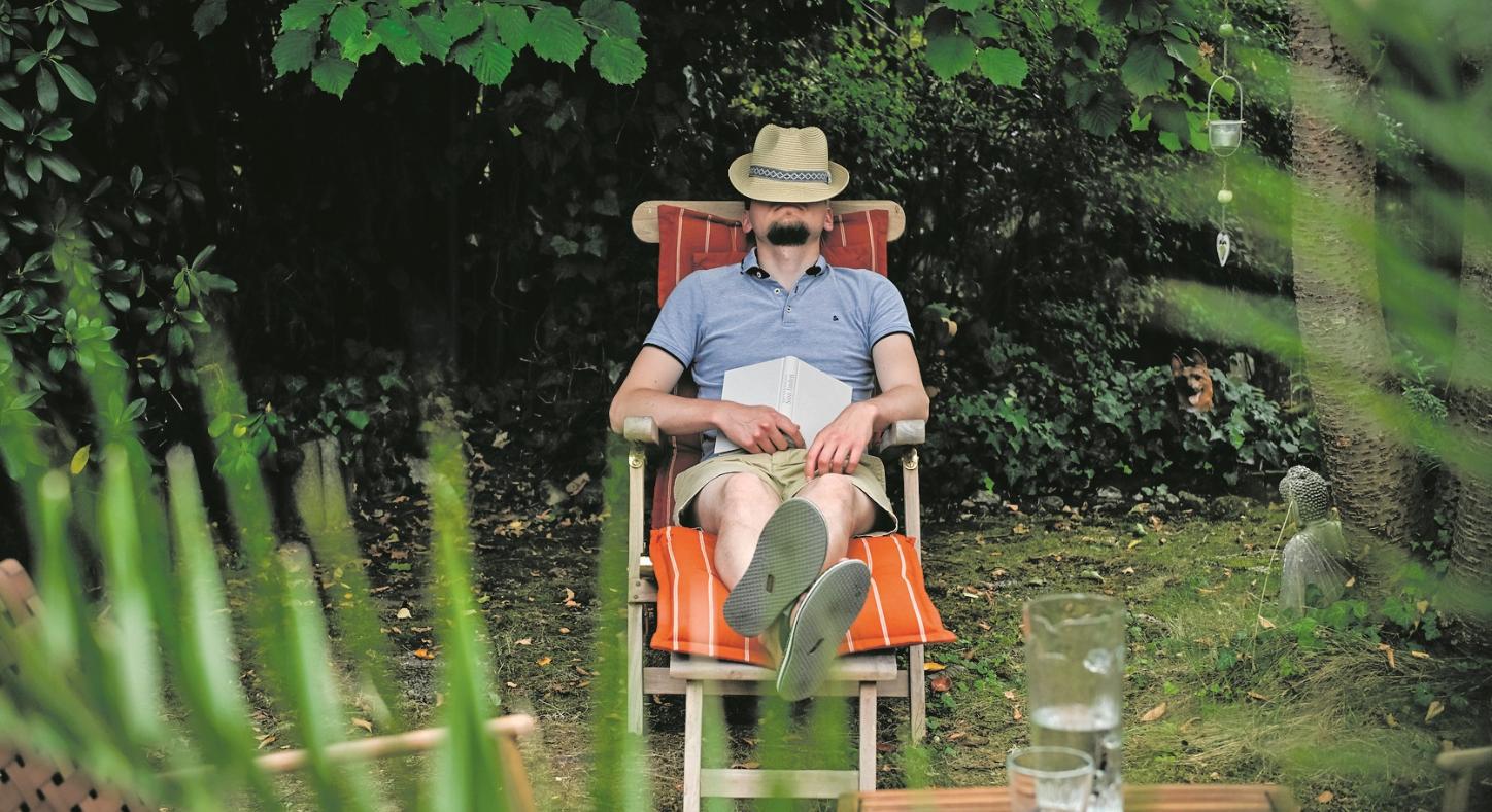 Ein Mann mit einem Hut auf dem Gesicht sitzt in einem Gartenstuhl und schläft, am 26. August 2025 in einem Garten in Bonn. Auf seinem Schoß liegt ein Buch.