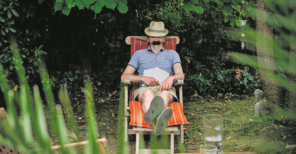 Ein Mann mit einem Hut auf dem Gesicht sitzt in einem Gartenstuhl und schläft, am 26. August 2025 in einem Garten in Bonn. Auf seinem Schoß liegt ein Buch.