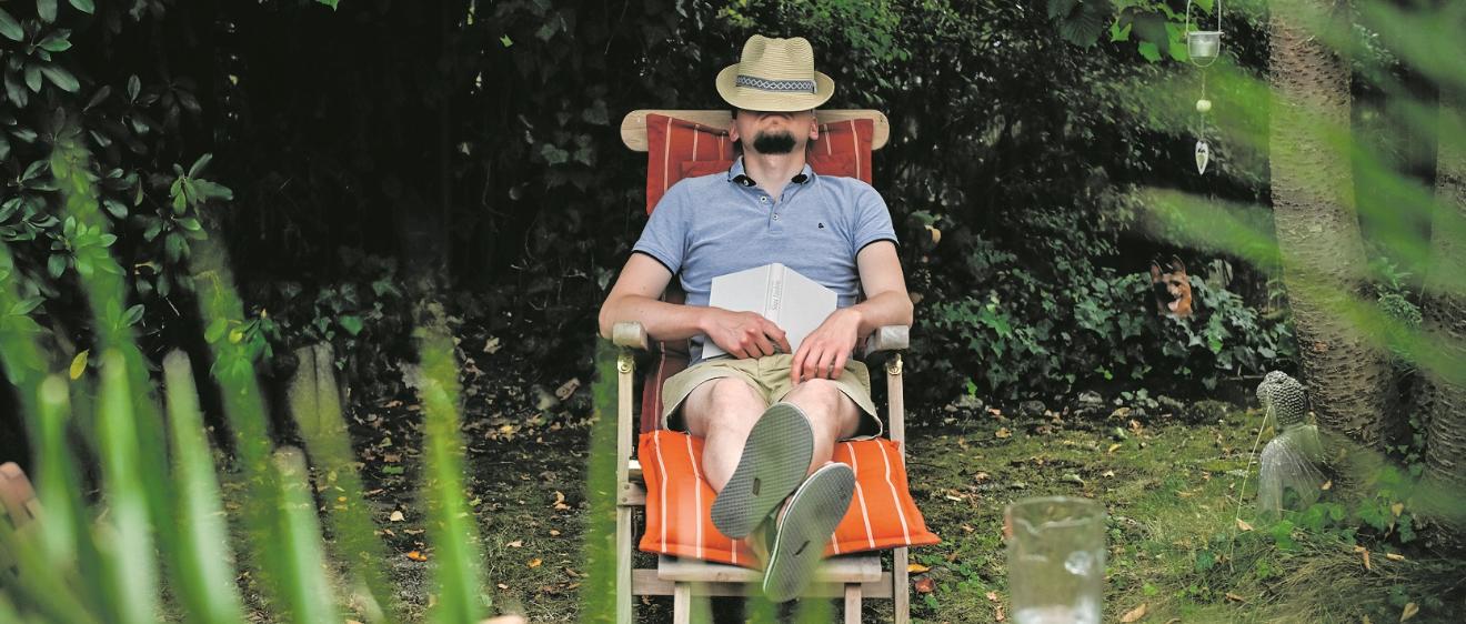 Ein Mann mit einem Hut auf dem Gesicht sitzt in einem Gartenstuhl und schläft, am 26. August 2025 in einem Garten in Bonn. Auf seinem Schoß liegt ein Buch.