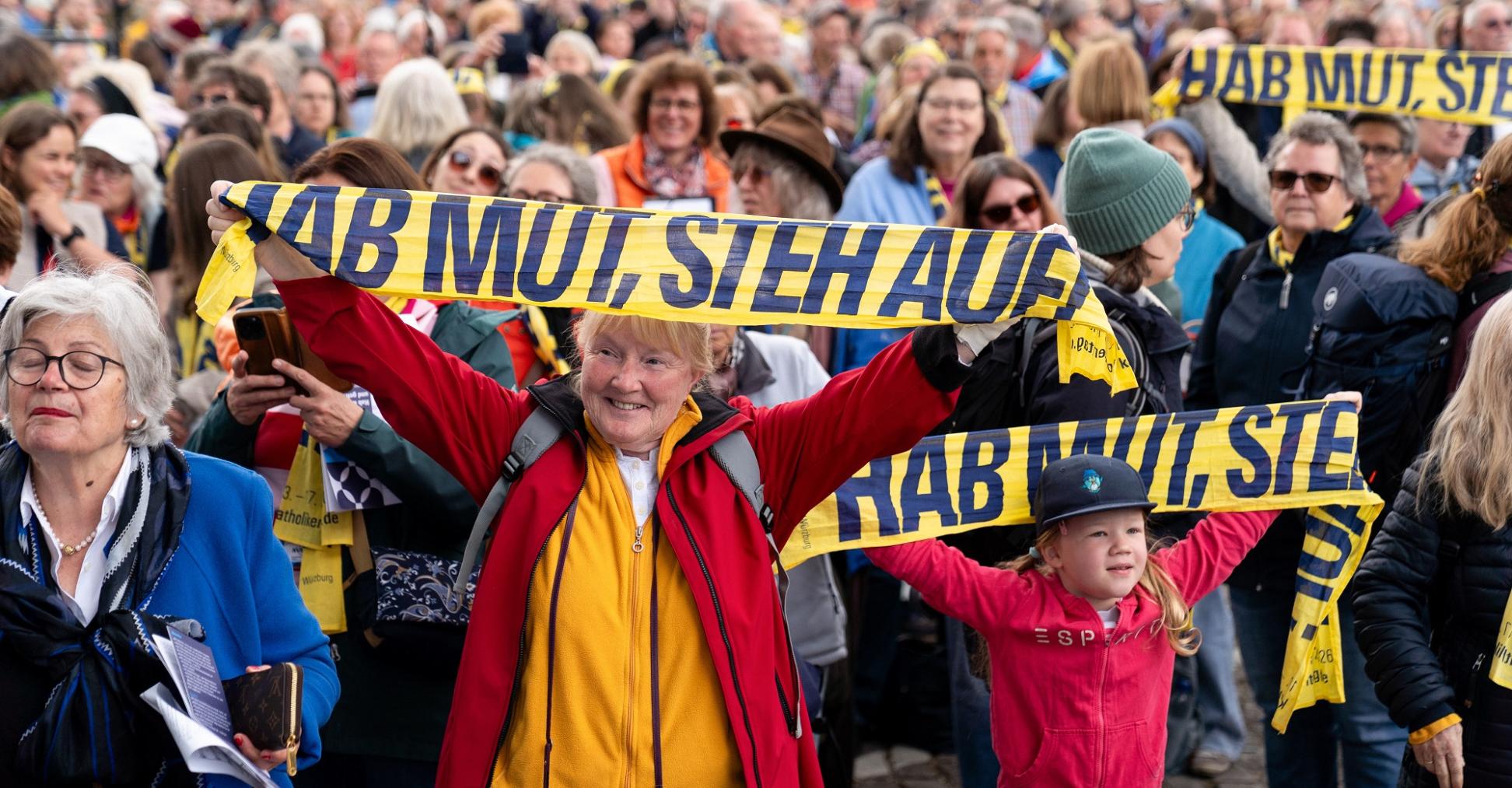 Teilnehmer halten Katholikentags-Schals hoch beim Abschlussgottesdienst am 17. Mai in Würzburg.