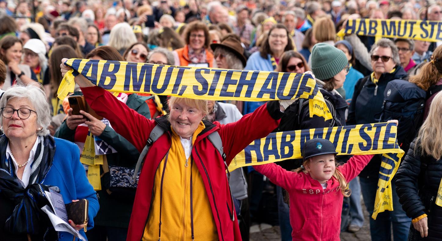 Teilnehmer halten Katholikentags-Schals hoch beim Abschlussgottesdienst am 17. Mai in Würzburg.