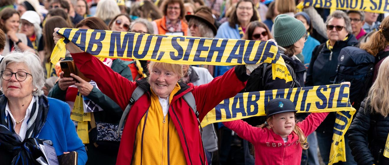 Teilnehmer halten Katholikentags-Schals hoch beim Abschlussgottesdienst am 17. Mai in Würzburg.