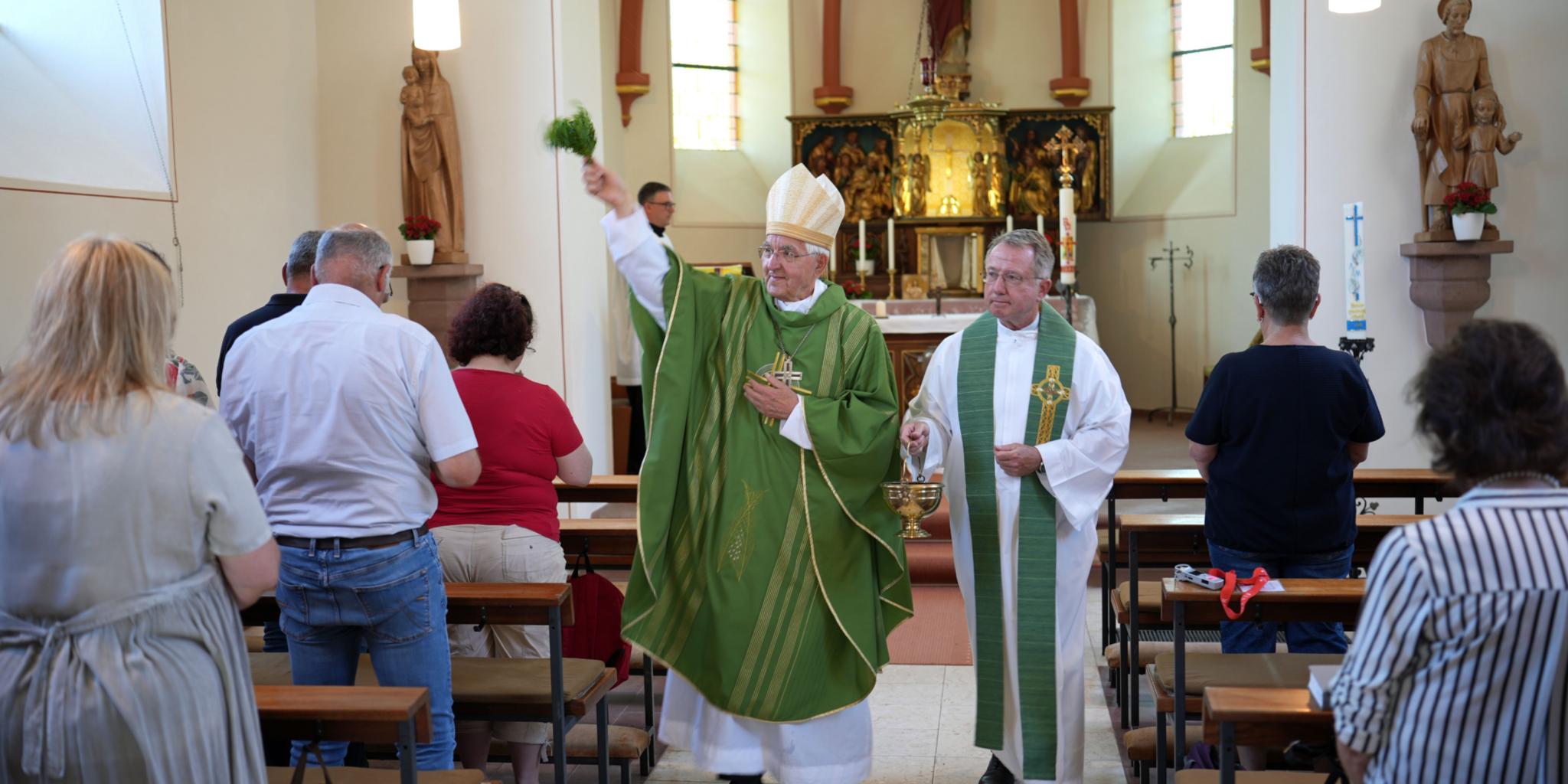 Weihbischof em. Gebert im Innenraum der Pfarrkirche; er segnet sie mit einem Palmzweig