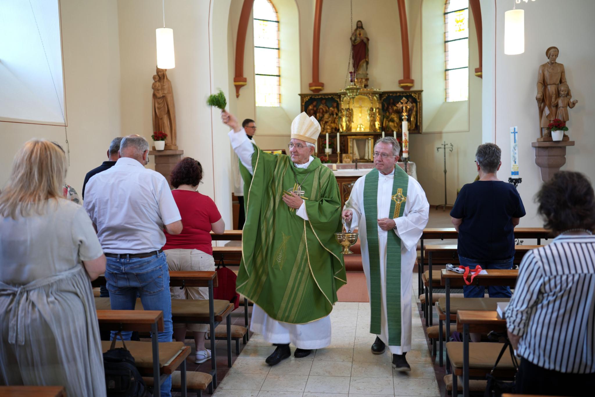 Weihbischof em. Gebert im Innenraum der Pfarrkirche; er segnet sie mit einem Palmzweig
