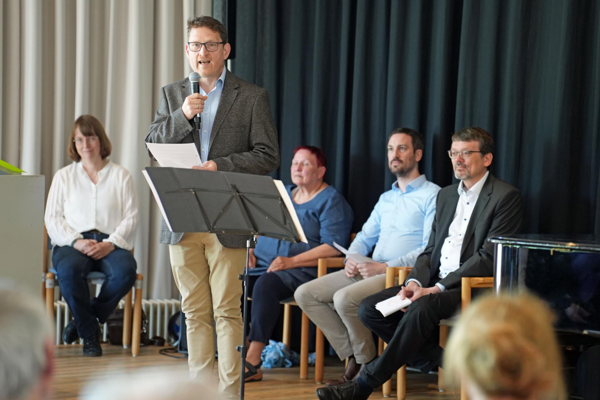 Roland Hinzmann (stehend) vom Leitungsteam des Pastoralen Raums Bernkastel-Kues mit Kooperationspartnerinnen und -partnern im Hintergrund: Monika Marmann, Uschi Fusenig, Tobias Schmitt und Pater Dr. Ralph Huning SVD (von links).