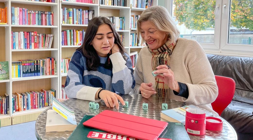Zwei Frauen spielen in einer Bibliothek gemeinsam ein Würfelspiel.