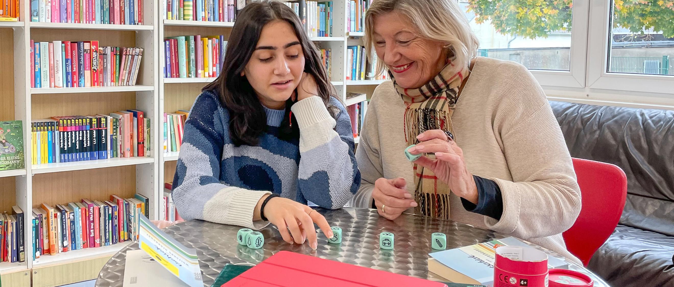 Zwei Frauen spielen in einer Bibliothek gemeinsam ein Würfelspiel.