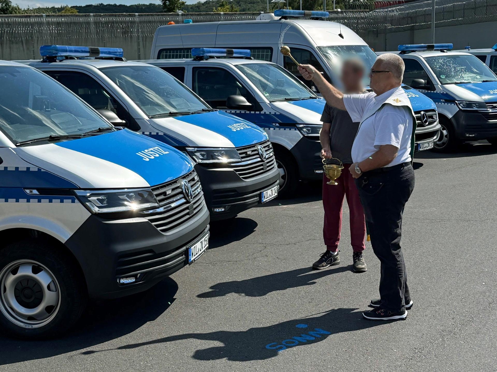 Diakon Thomas Reichert segnet die Einsatzfahrzeuge der Justizvollzugsbeamten und einen Krankentransporter